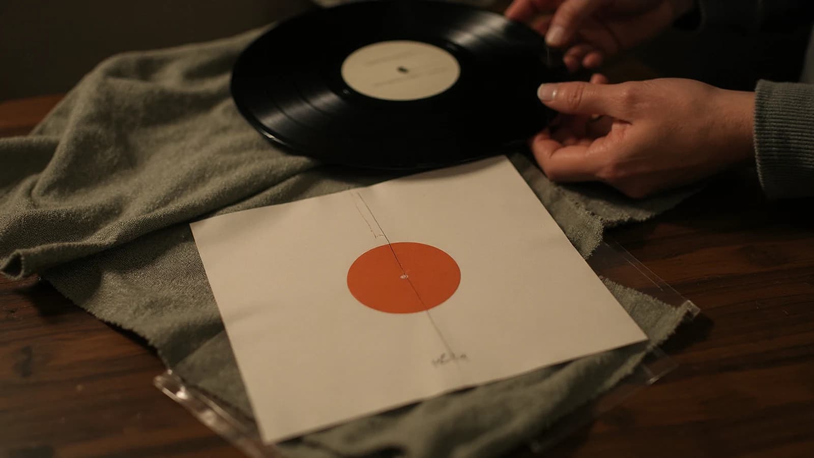 A vinyl record and its protective sleeve being handled with care on a wooden surface.
